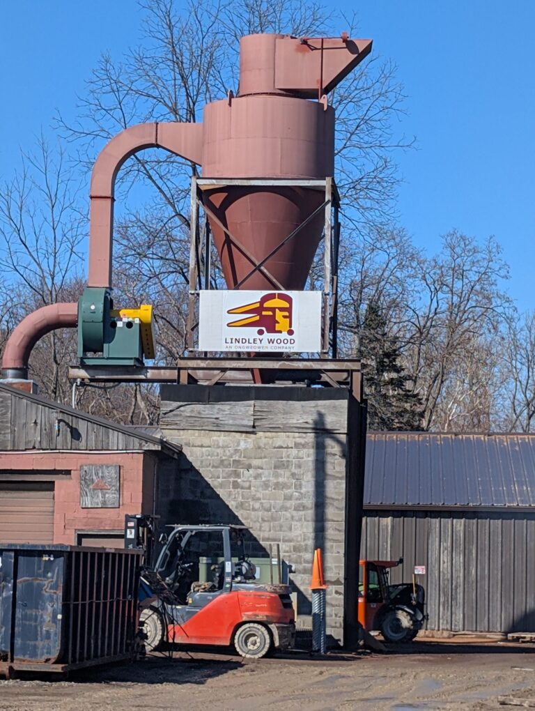 Rust-red cyclone dust collector fabricated and installed by AM Metal on a rooftop steel platform at a pallet manufacturing plant.