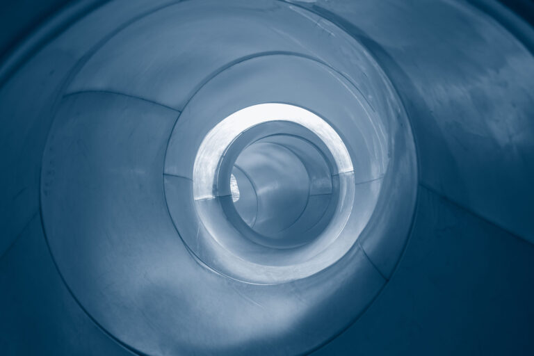 View from inside a spiraling, circular tunnel or tube slide with smooth metallic surfaces and shades of blue—showcasing depth and perspective toward a bright opening, this scene evokes cutting-edge industrial design services.